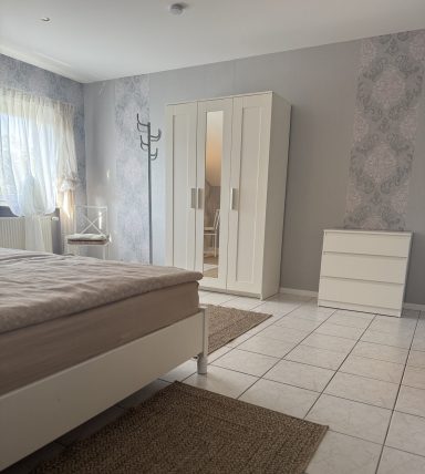 Helles Schlafzimmer mit einem Bett, einem Schrank, einem Kasten und Teppichen.