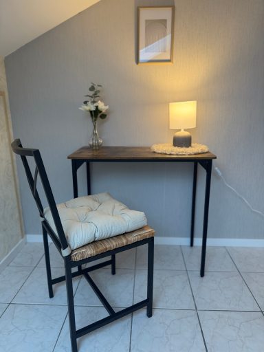 Ein kleiner Schreibtisch mit einer Lampe, Stuhl und einer blühenden Dekoration.