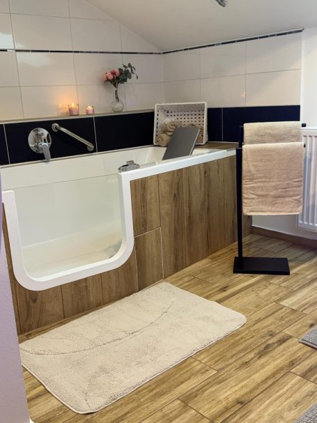 Modernes Badezimmer mit Badewanne, Holzoptik und Handtüchern auf einem Halter.