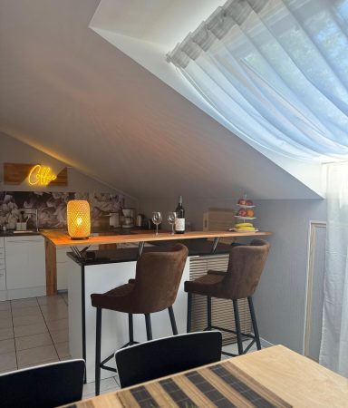 Heller Raum mit Barhockern, Theke und Lichtquelle unter schräger Decke.