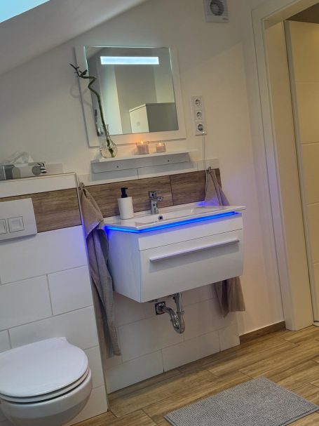 Modernes Badezimmer mit Waschtisch, Spiegel und sanfter Beleuchtung.